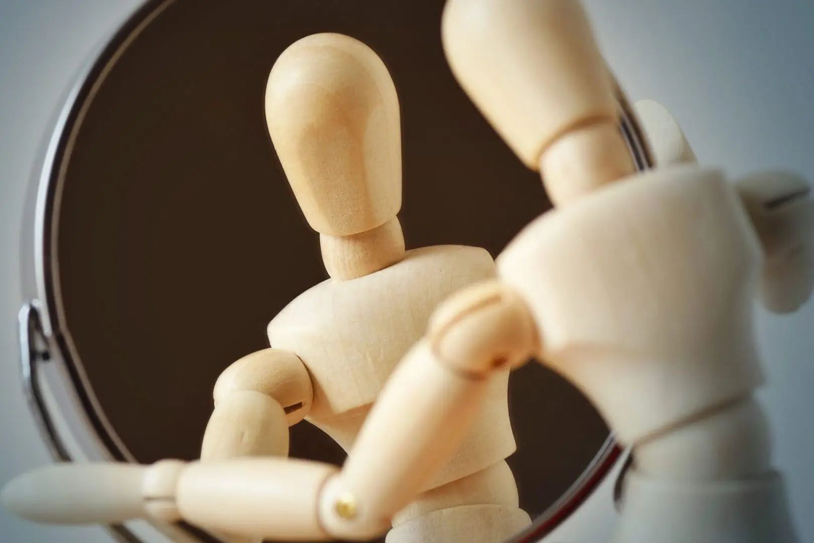 A wooden doll is in front of a mirror.